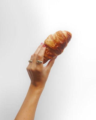 Saint Croissant ring worn: hand holding a croissant, wearing gold rings