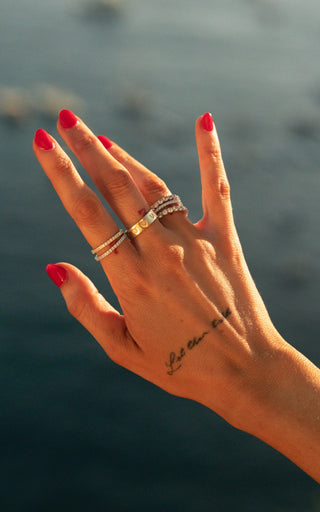 Close-up of a hand raised against the ocean wearing stacked silver and gold IKAIKA rings
