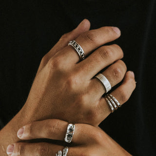 This Too Shall Pass ring worn: hands wearing silver rings against a black background