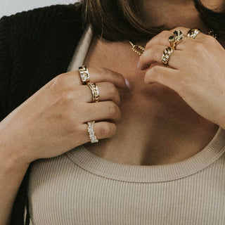 Her Tears ring worn: hands at the collarbone wearing stacked gold rings