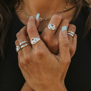 Metamorphosis ring worn: hands crossed over the chest, wearing silver butterfly rings and a gold chain necklace