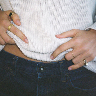 Stacker ring worn: person in a white knit sweater and jeans wearing stacked rings