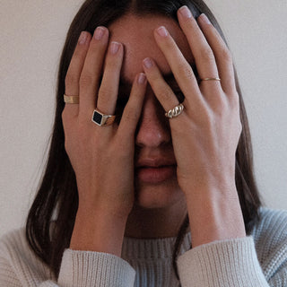 The Moment ring worn: person covering their face, wearing a black stone signet