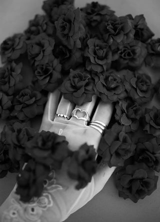 Love Language ring worn: black and white photo of a hand wearing silver rings among dark roses