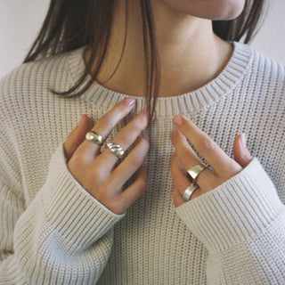 Saint Croissant ring worn: person in a knit sweater, hands at the chest wearing gold and silver rings